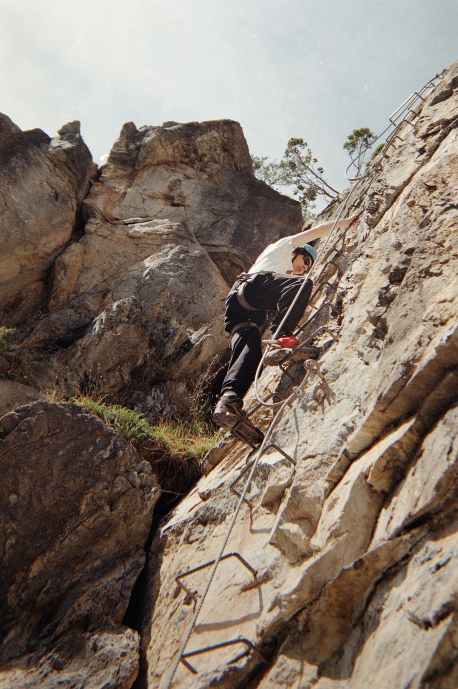 It would be crazy hard to climb this, near-vertical chunk of rock. Fortunately we are doing a Via-ferrata, and convenient poles of steel have been incrusted in the cliff, forming a ladder. Lil'brother is having a go at it, wearing the perfectly adequate equipment: hiking shoes, blue helmet, sunglasses, pant and obvisouly his climbing harness.