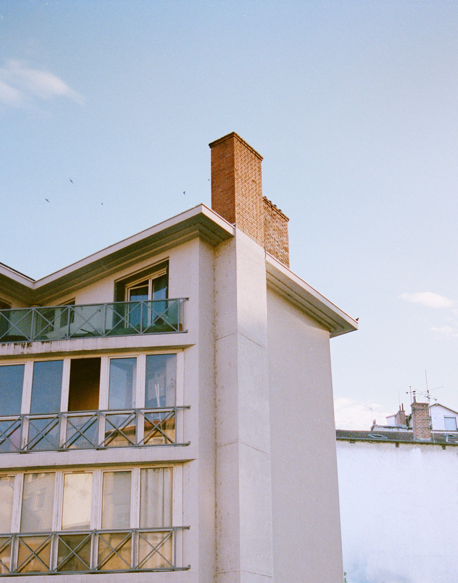 It's the end of a hot summer day. A tired sun is brushing the top of taller buildings in its warmth. Swallows are swimming through the big blue sky spotted with delicate cloud clumps. I pointed the camera up, that building had the perfect lighting, with a sun beaming perfectly the beautiful brick chimney at its top.